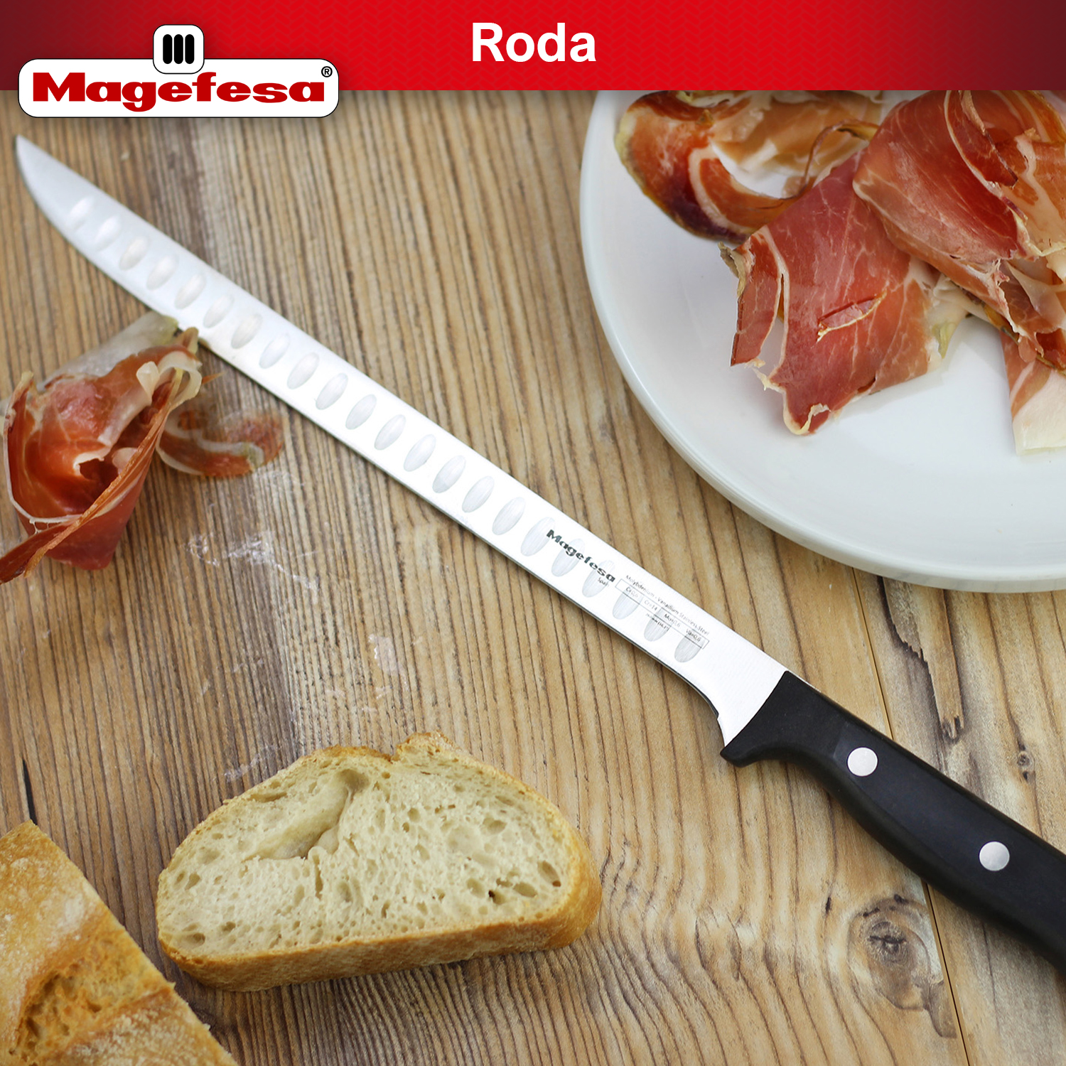 Un cuchillo largo y delgado con mango negro yace junto a pan y jamón sobre una mesa de madera.