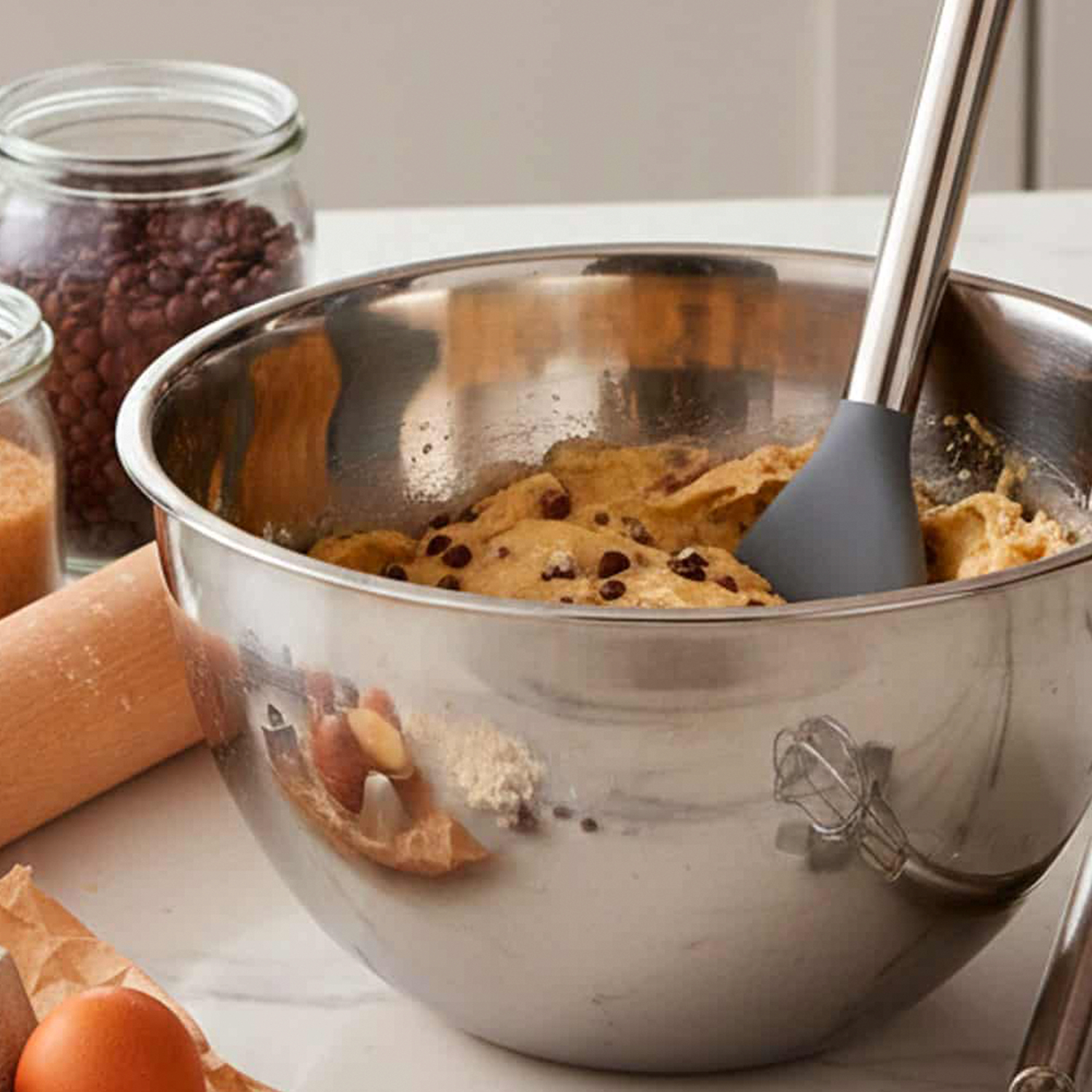 Bol de acero inoxidable con masa de galleta y chispas de chocolate, rodeado de ingredientes.