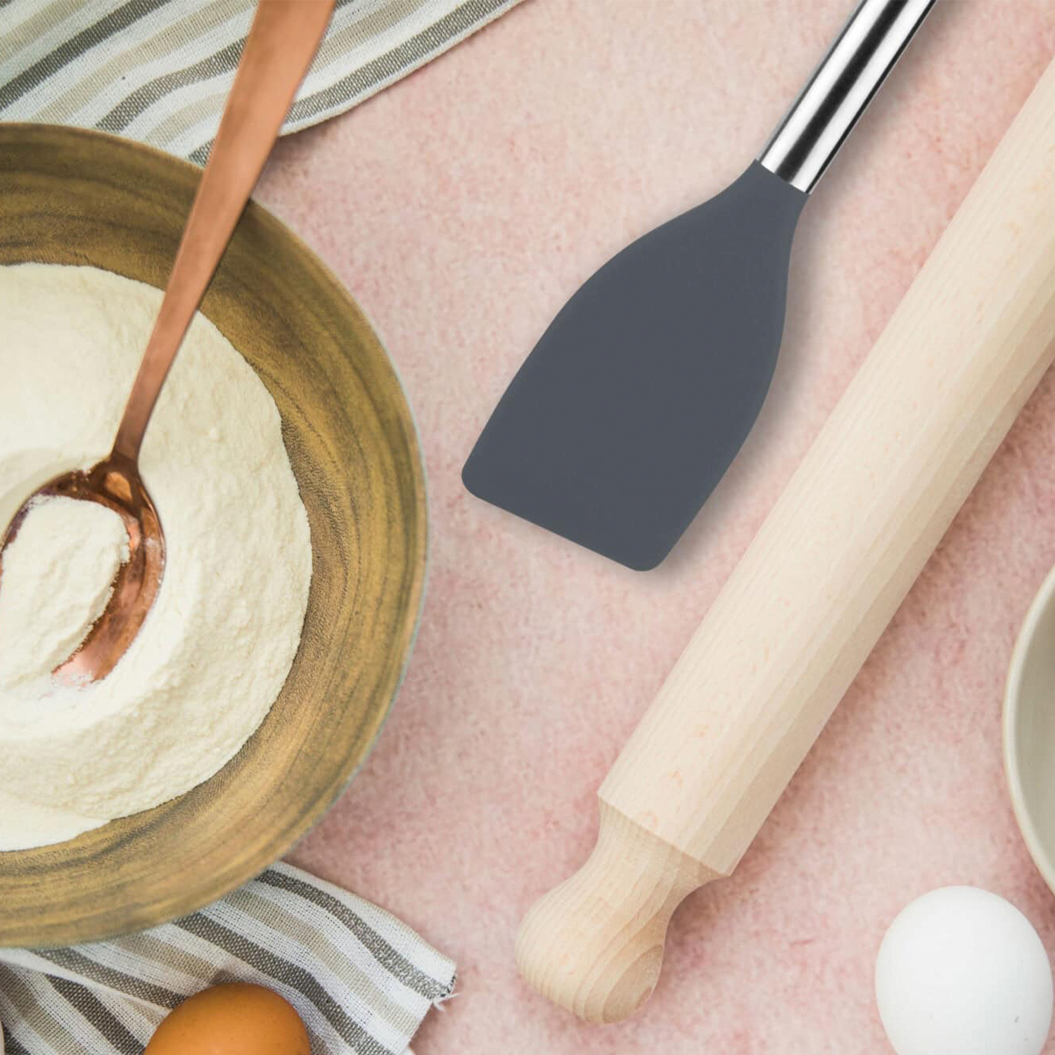 Ingredientes para hornear: Harina en bol, espátula, rodillo, huevos sobre superficie rosa.