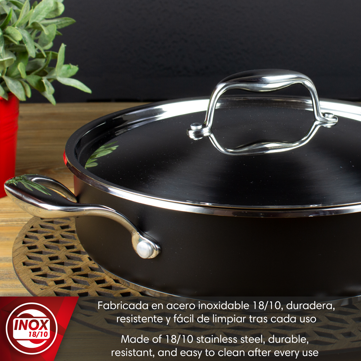 Olla negra con tapa y asa de acero inoxidable, junto a una planta.