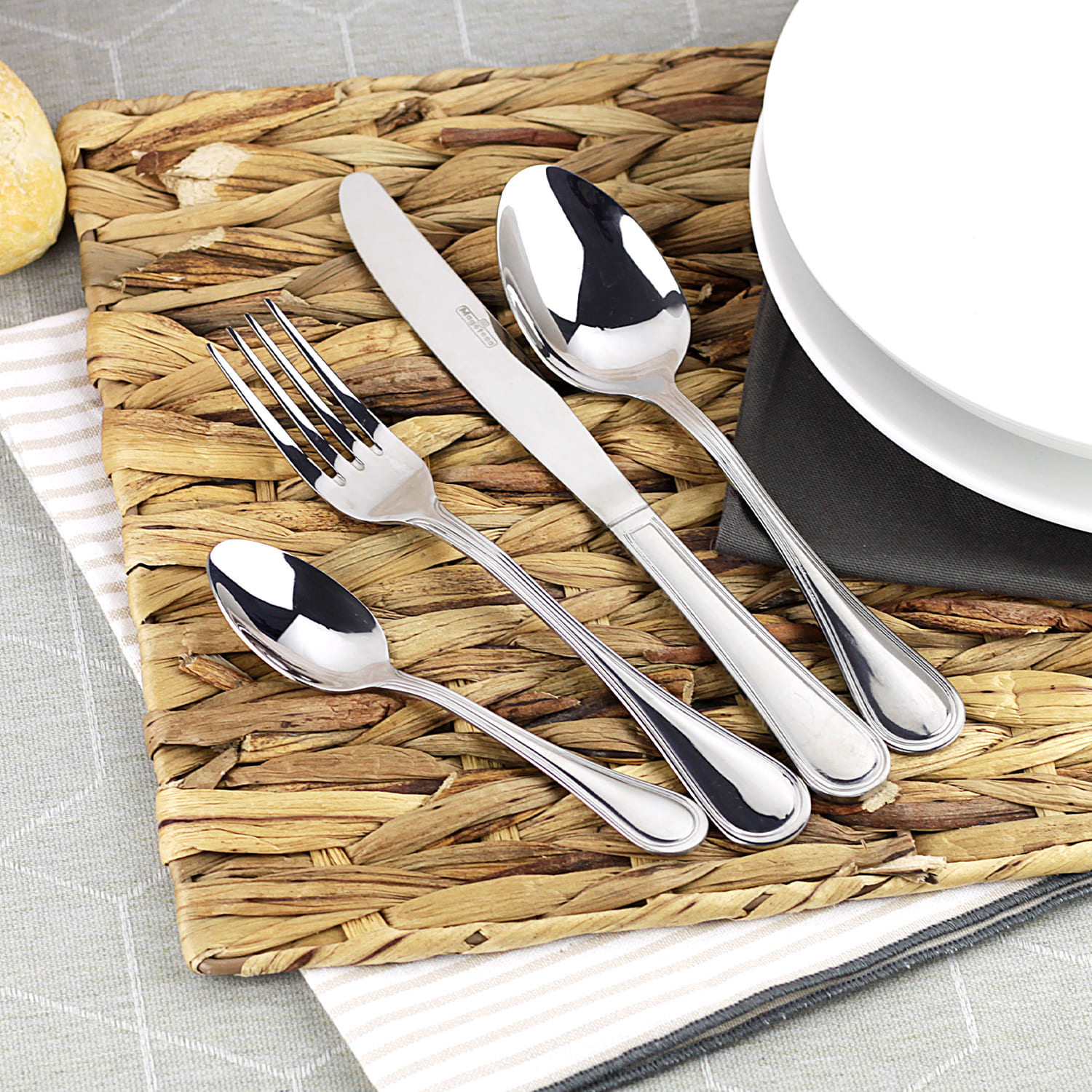 Juego de cubiertos sobre un mantel individual tejido con plato blanco y panecillo.