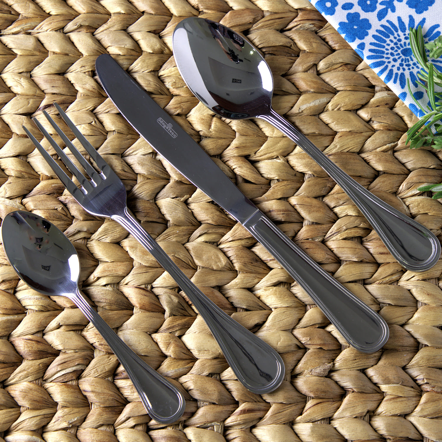 Cubiertos: cuchillo, tenedor y cucharas sobre una alfombrilla tejida.