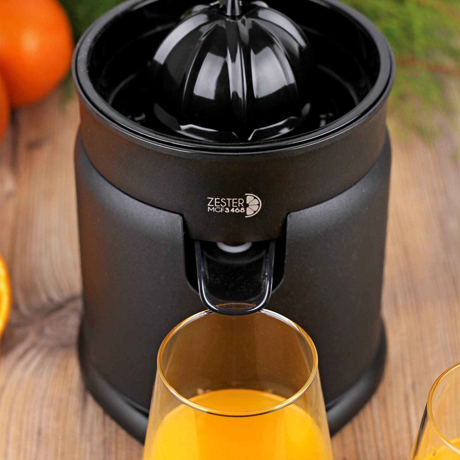 Un exprimidor eléctrico negro sobre una mesa de madera con dos vasos de zumo de naranja.