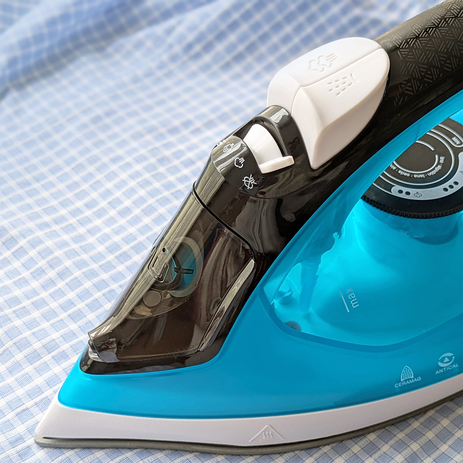 Una plancha de vapor azul descansa sobre tela de cuadros azules.