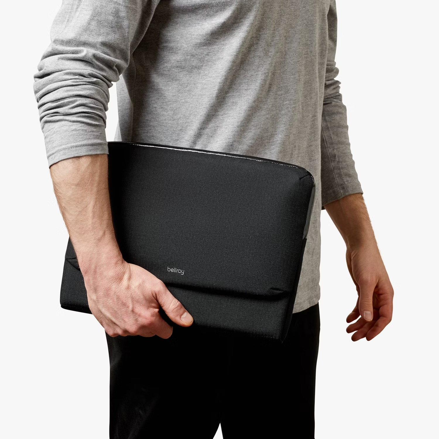 Un uomo con maglia grigia a maniche lunghe tiene una borsa nera per laptop.