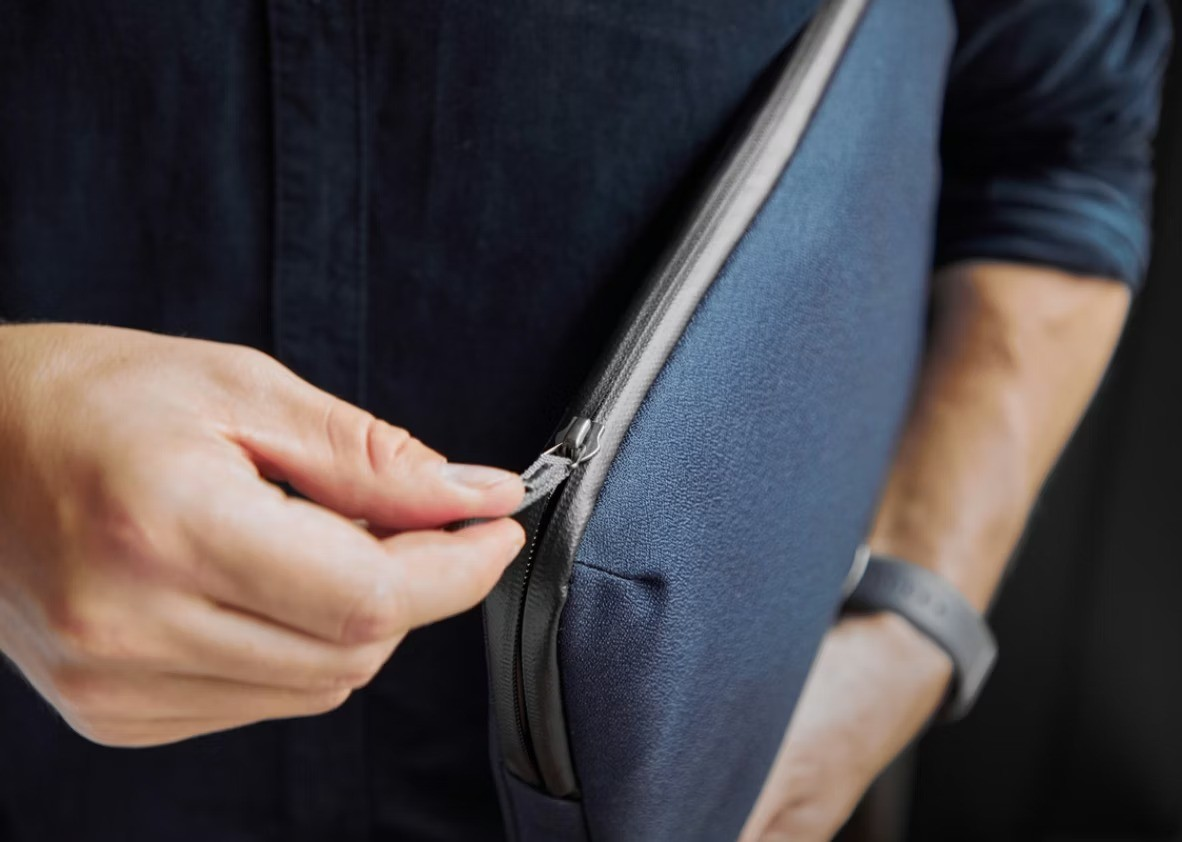 Una mano chiude la cerniera di una custodia blu scuro per laptop tenuta da una persona.