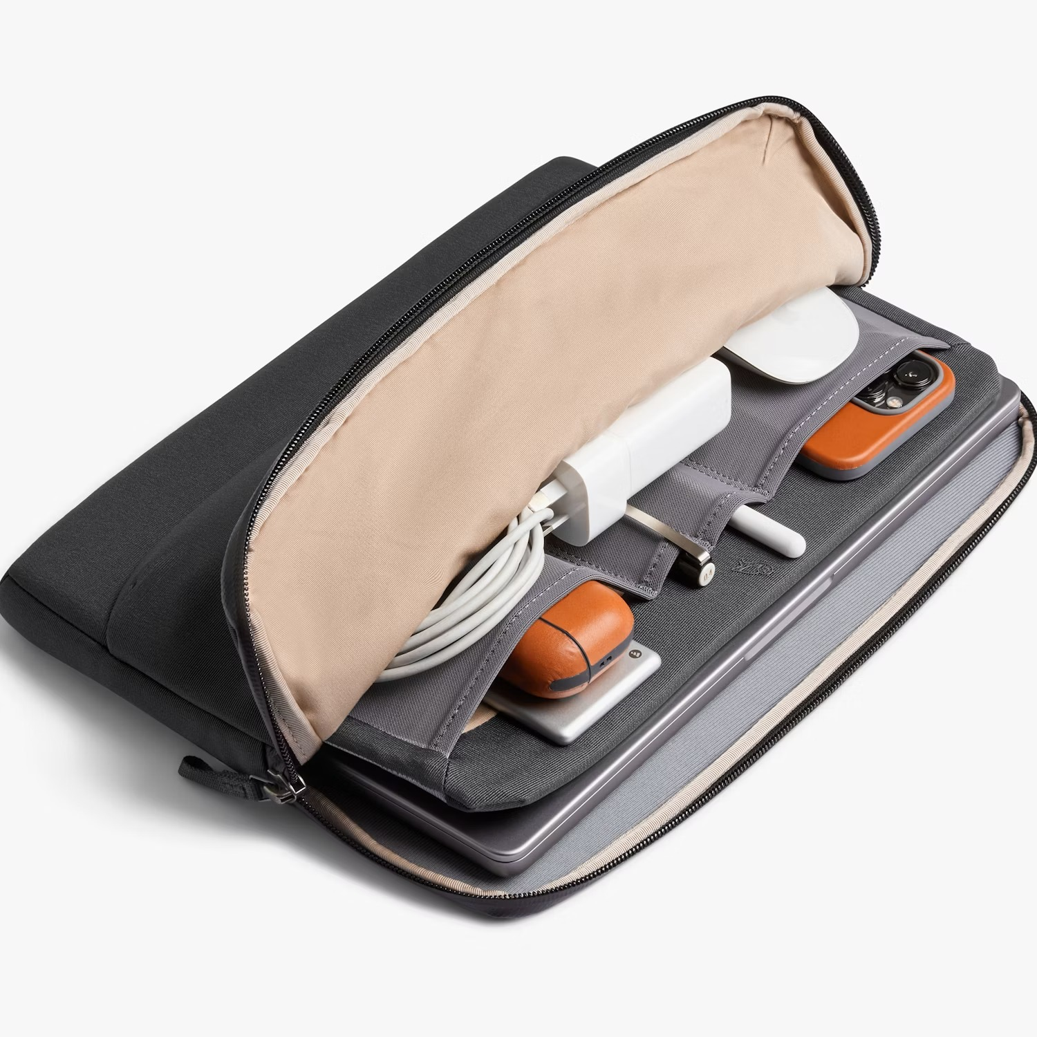 Een donkere tas vol technologie: oplader, muis, telefoon, AirPods en laptop.