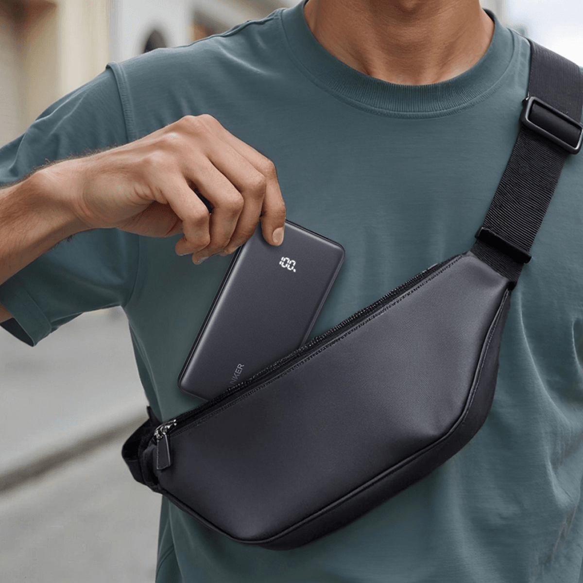 Hombre con camiseta gris mete power bank en riñonera negra.