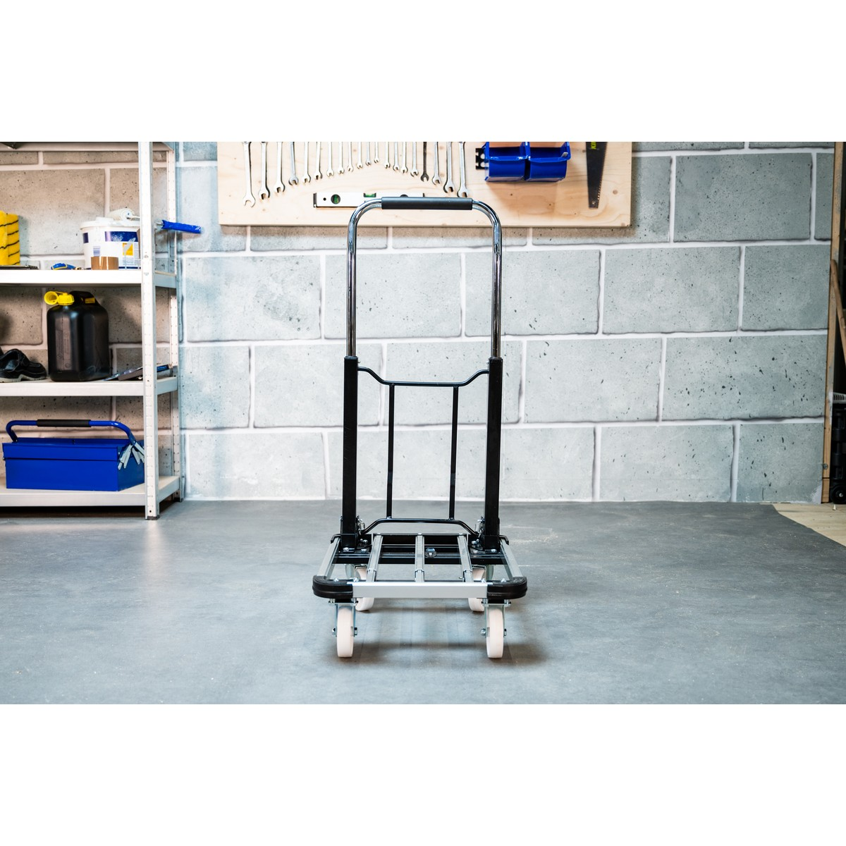 A foldable hand trolley with a silver frame and black handles stands on concrete.