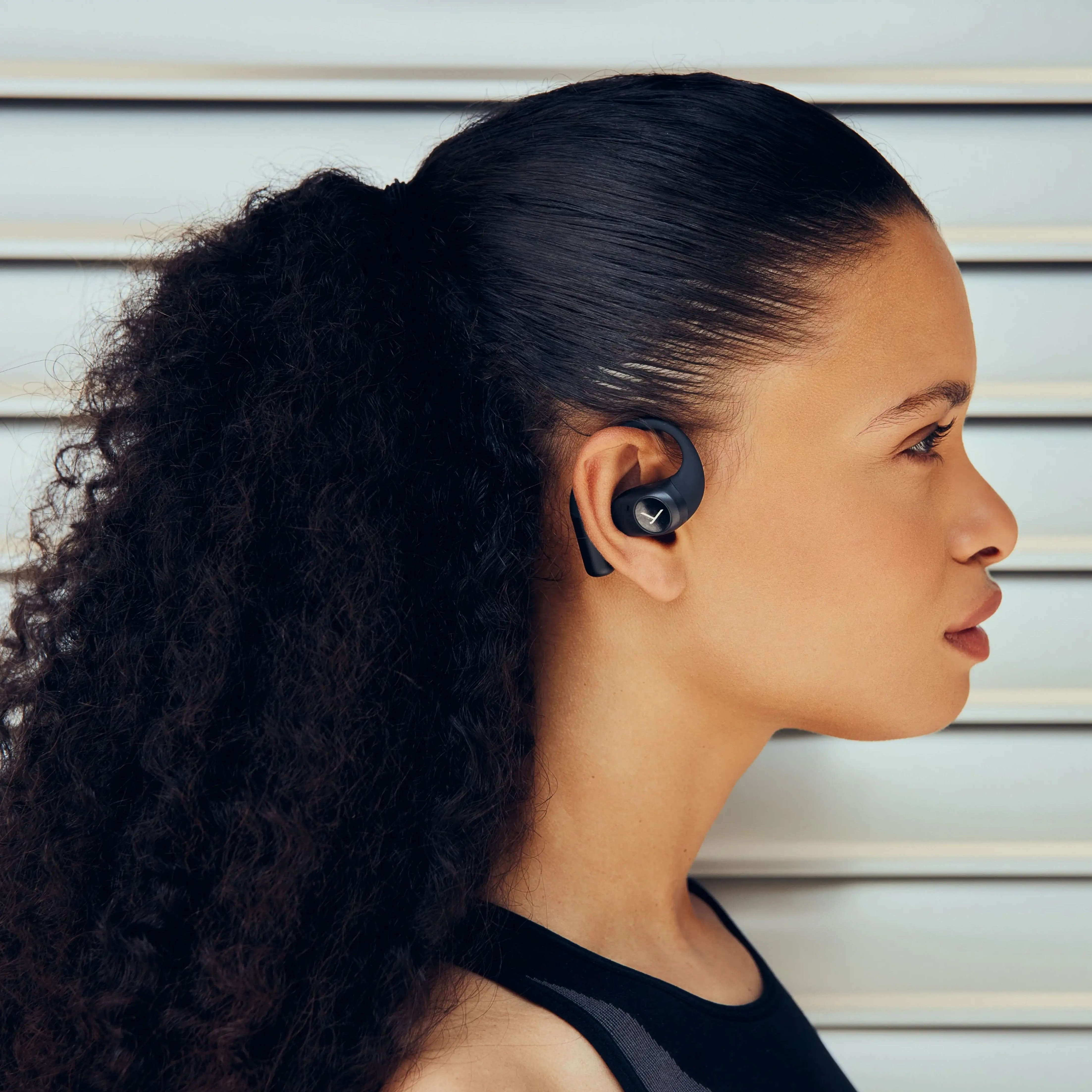 Femme aux cheveux noirs avec écouteurs à l'oreille droite, de profil.