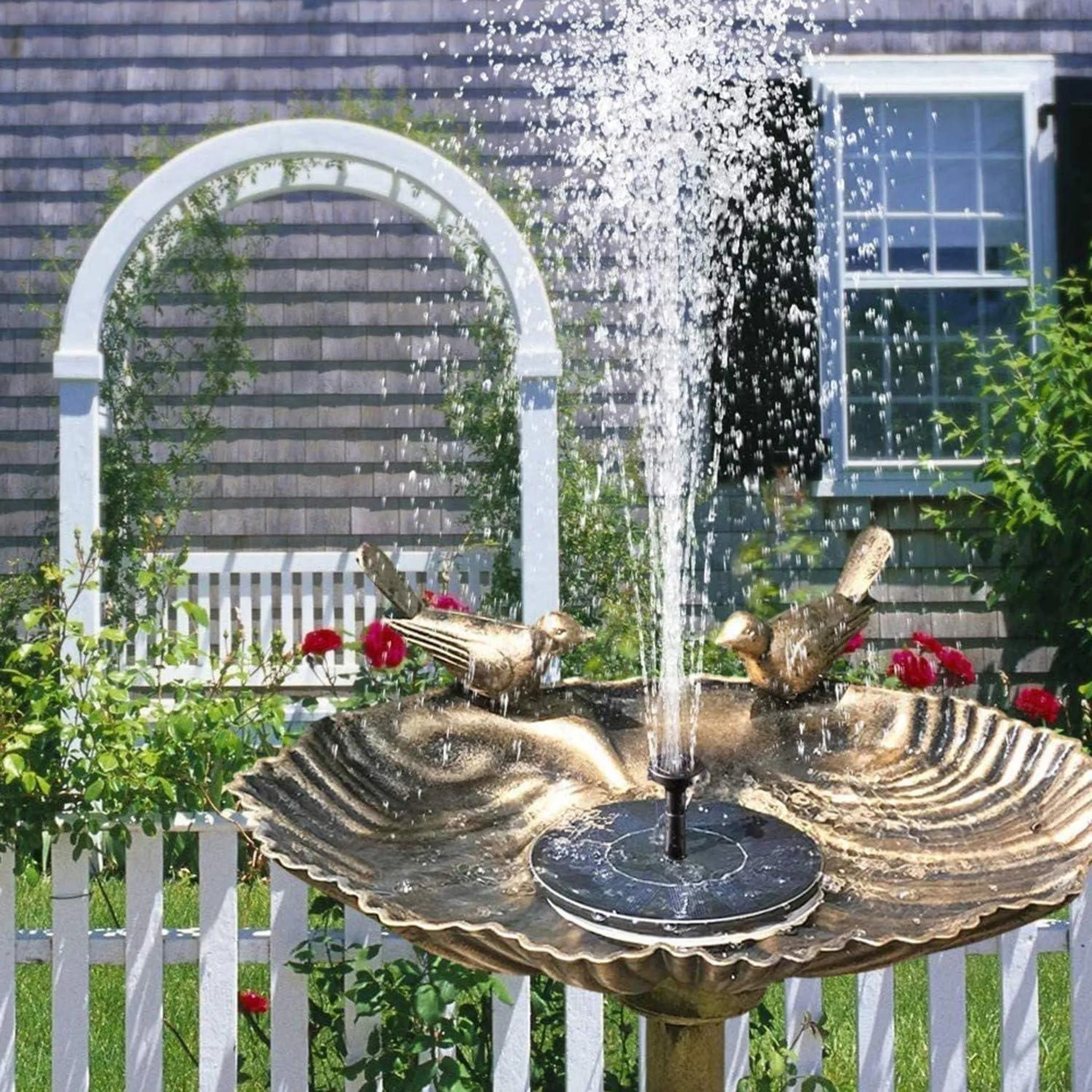 Ein Vogelbad-Brunnen mit Wasserfontäne und Vogeldekorationen vor einem Haus.