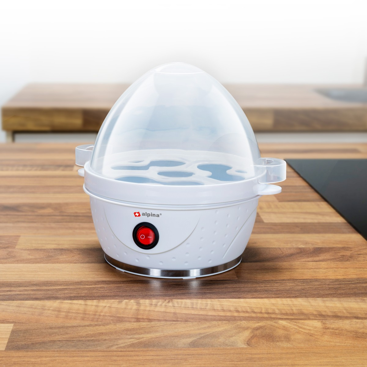 A white egg cooker with a clear lid sits on a wooden countertop.