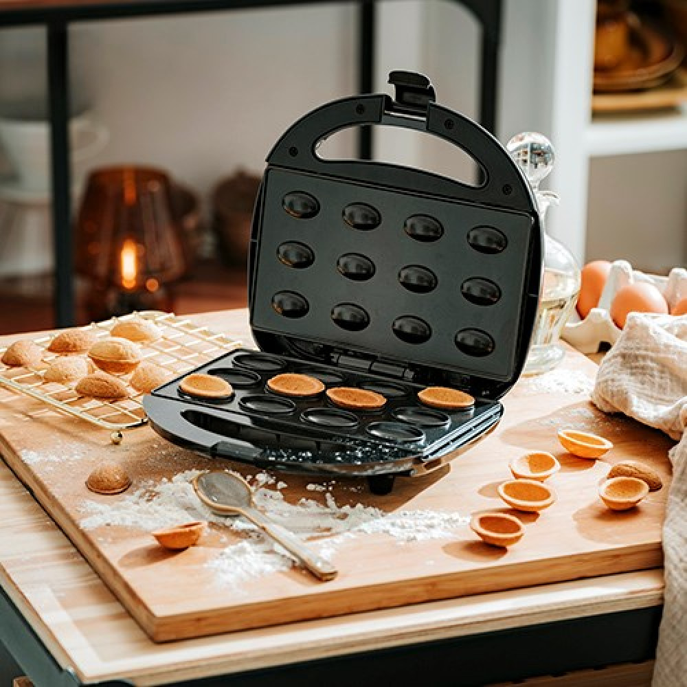 Una piastra per waffle nera con pastella in alcuni stampi. Biscotti su una gratella.