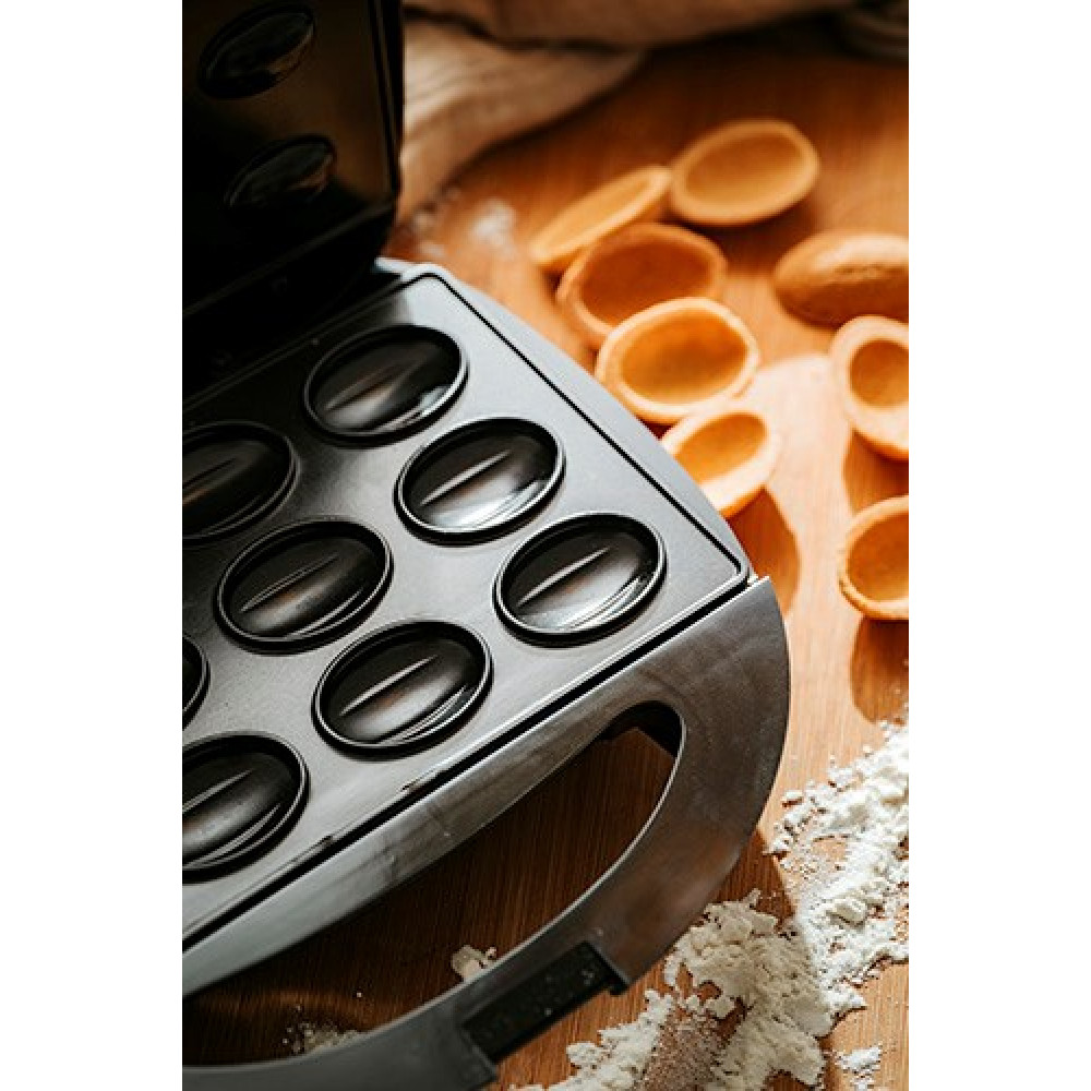 Una piastra per waffle aperta con stampi rotondi e gusci di pasta dorati accanto.