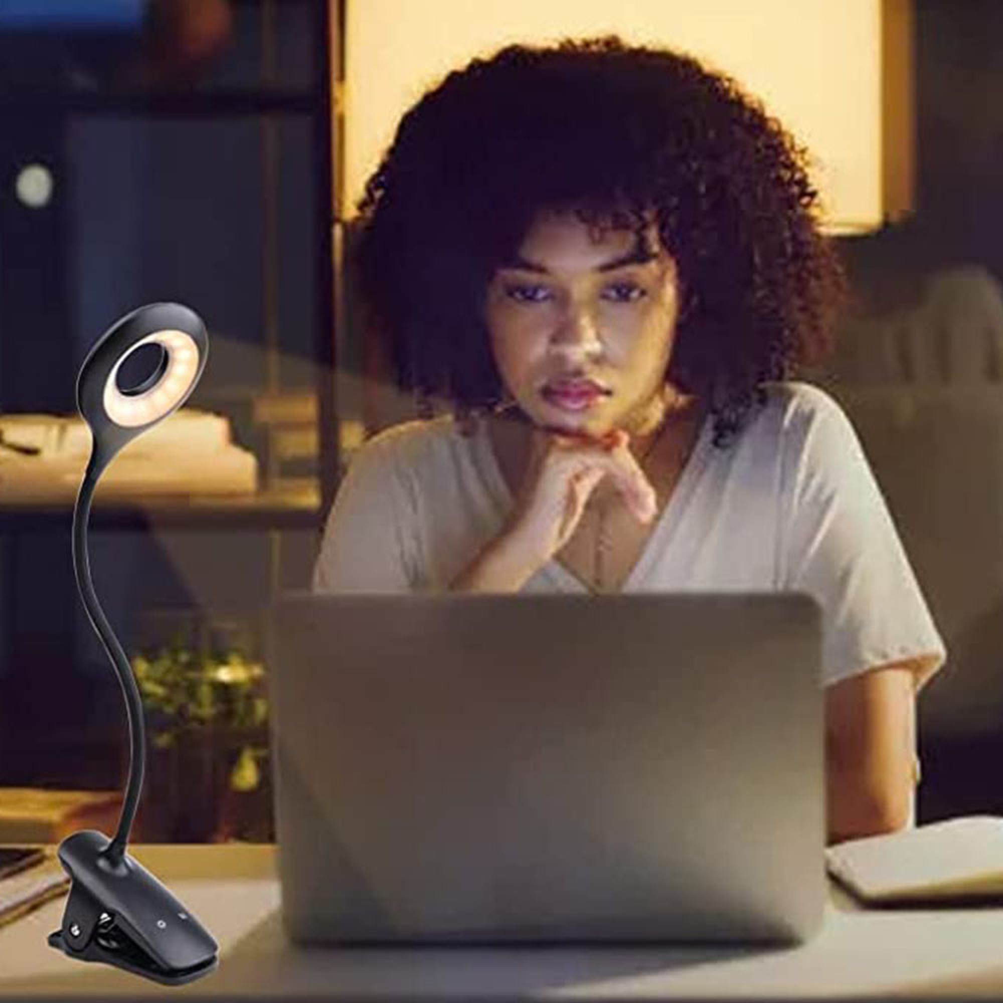 Eine Frau mit lockigem Haar blickt auf einen Laptop, eine Klemmlampe ist in der Nähe.