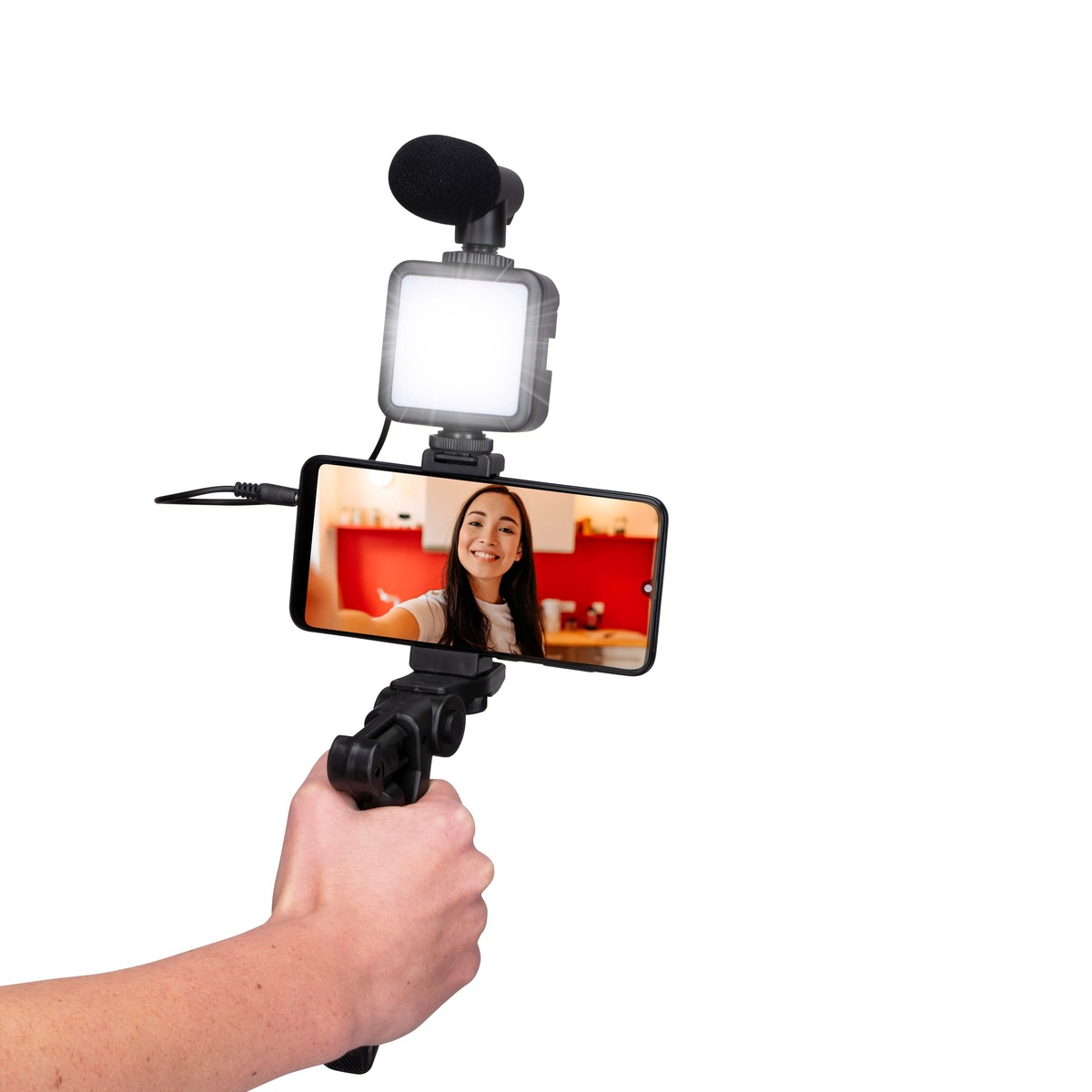 Person holds smartphone with mic & light, showing smiling face on screen.
