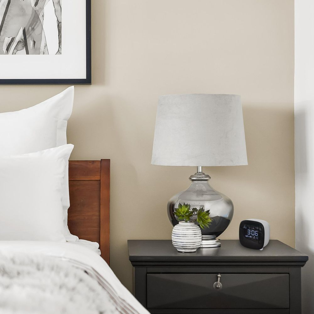 Un comodino con lampada, orologio e vaso accanto a un letto.