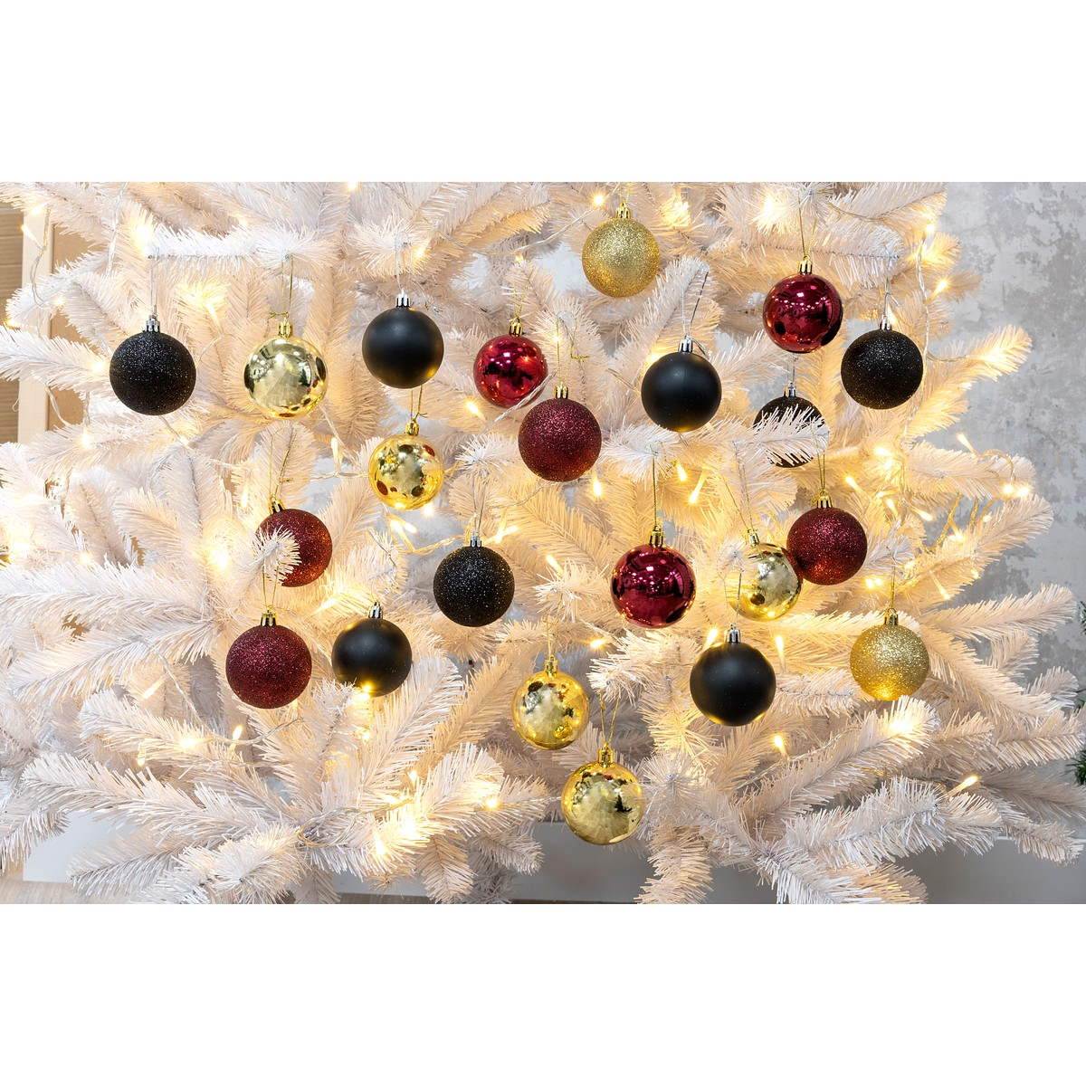 A white Christmas tree adorned with lights and red, black, and gold baubles.