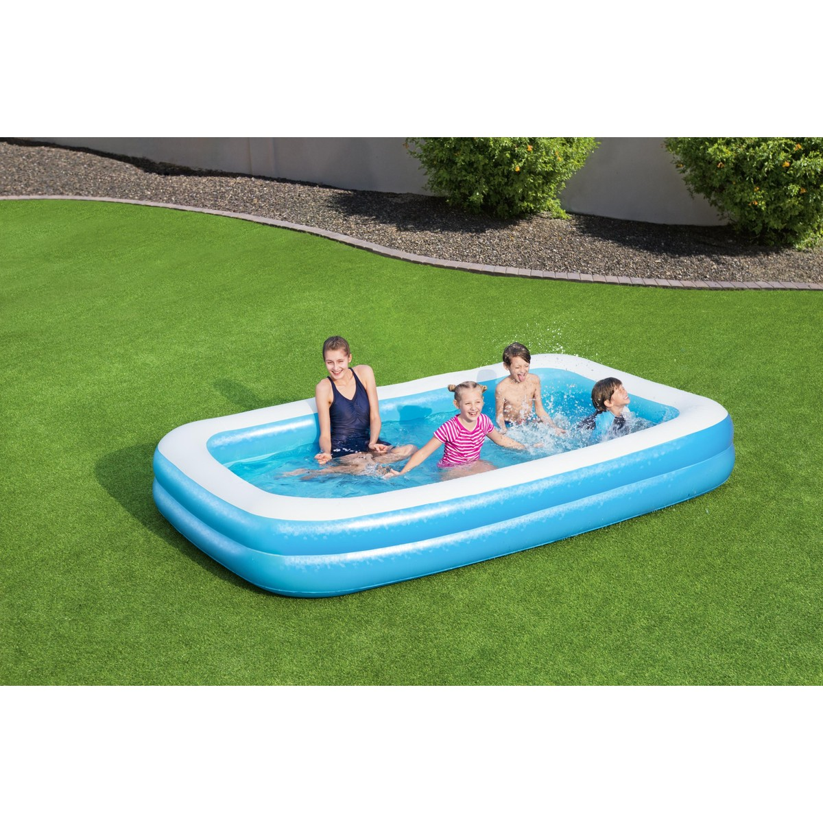 Quattro bambini, inclusa una bambina con un top a righe rosa, sguazzano e giocano in una piscina gonfiabile blu su un prato verde.
