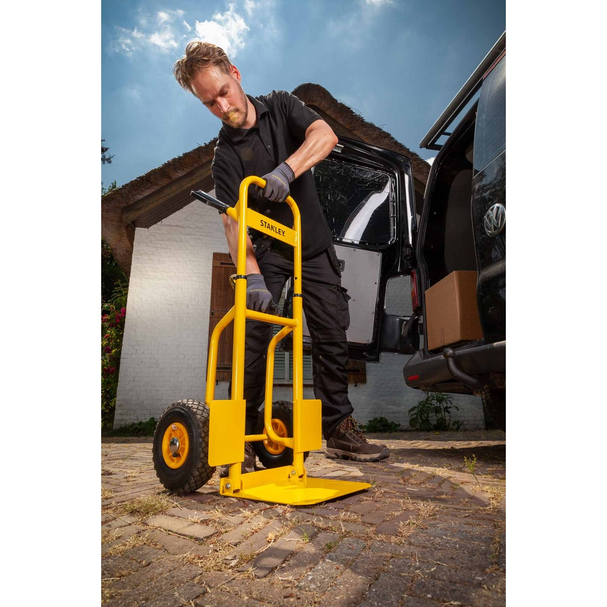 Man with yellow hand truck loading boxes into a black van.