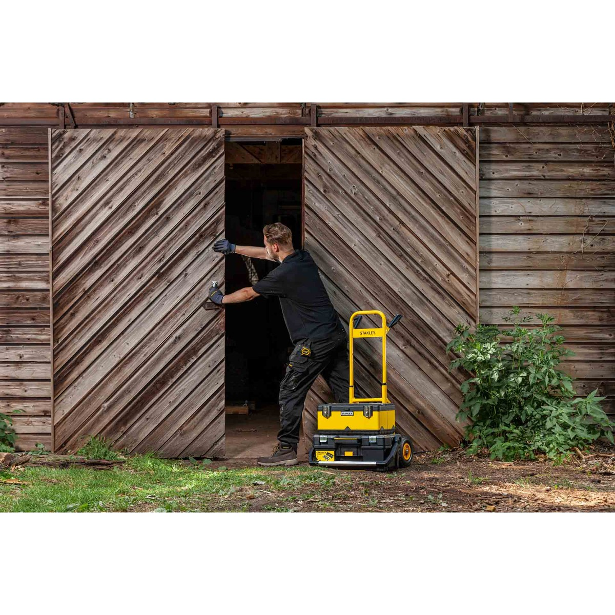 A man opens a wooden door, with a yellow tool cart next to him.