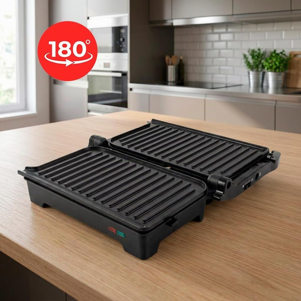 Una griglia a contatto nera aperta è su un tavolo di legno. Una cucina sullo sfondo.