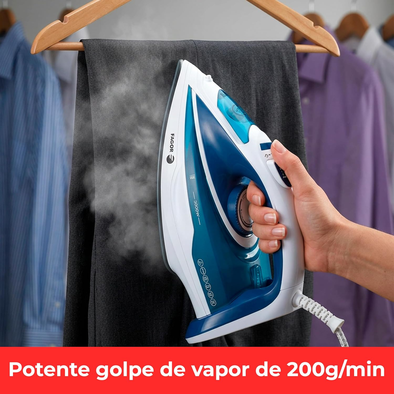 Una mano tiene un ferro da stiro che spruzza vapore su pantaloni scuri. Vestiti appesi sullo sfondo.