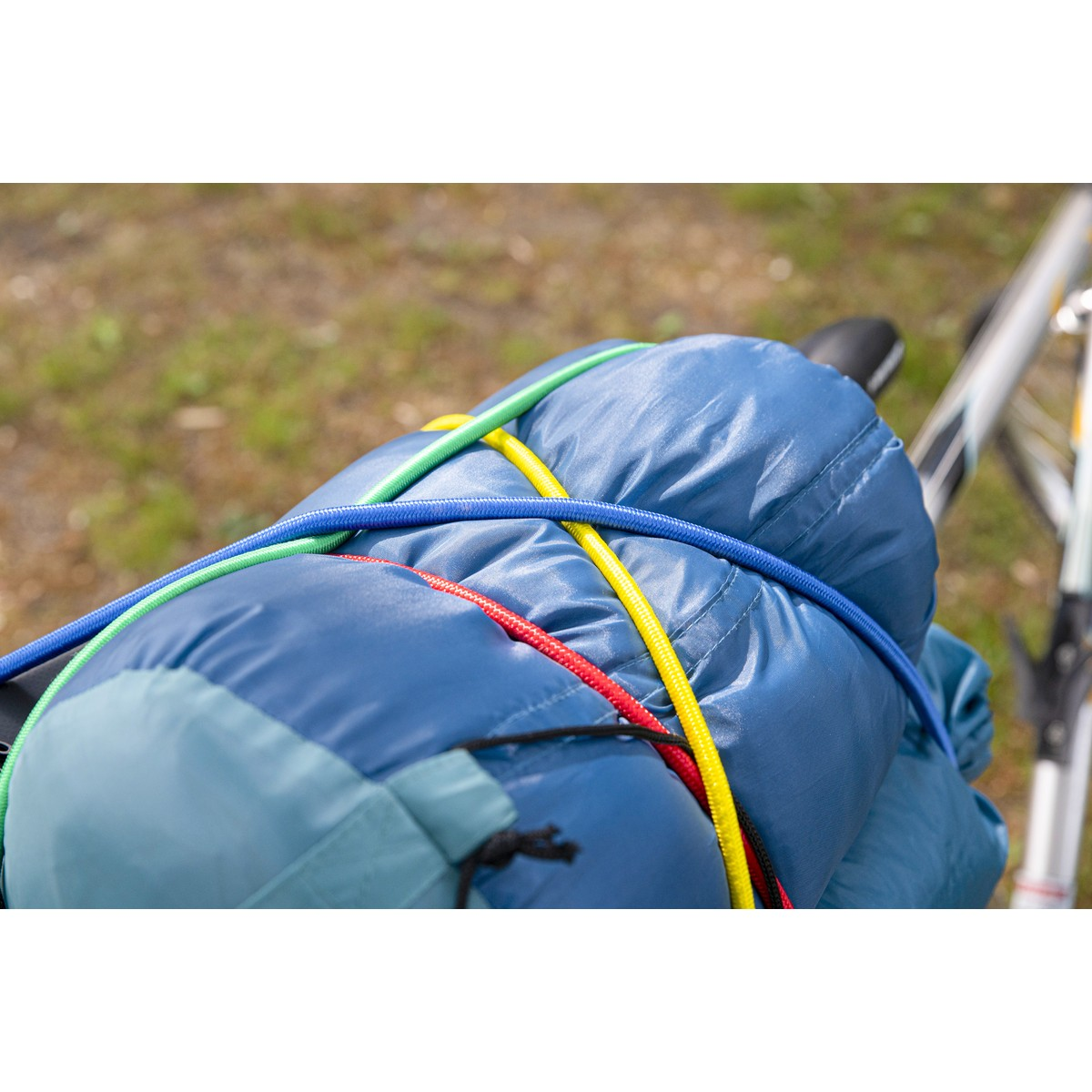 Blauwe slaapzak vastgezet met kleurrijke elastische koorden op een fiets.