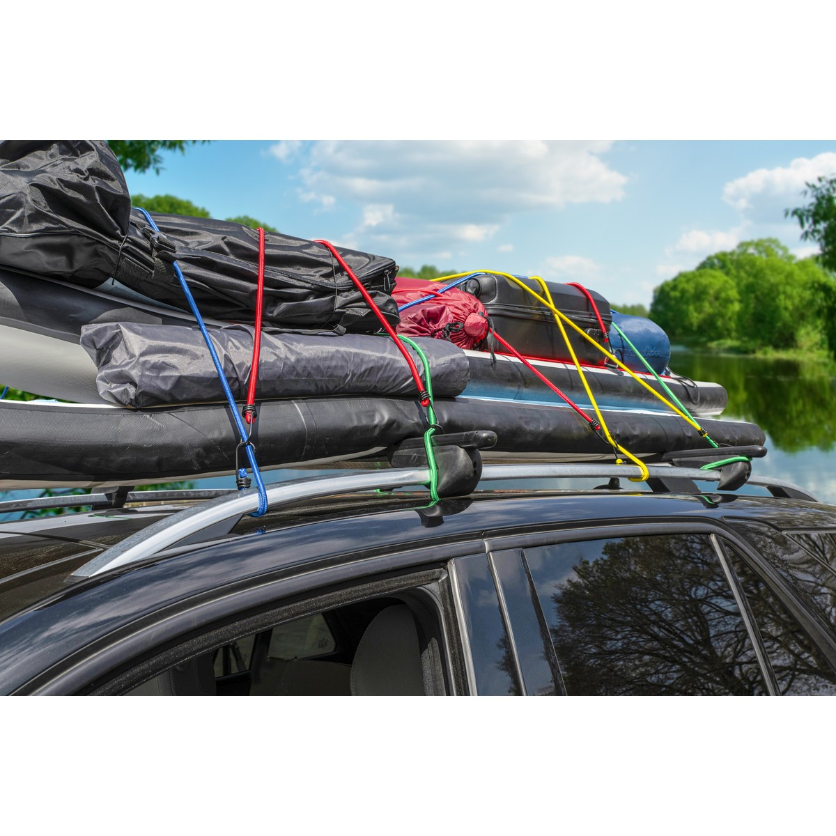 Zwarte imperiaal op dak van auto beladen met spullen, vastgezet met kleurrijke elastieken. Meer en bomen op achtergrond.
