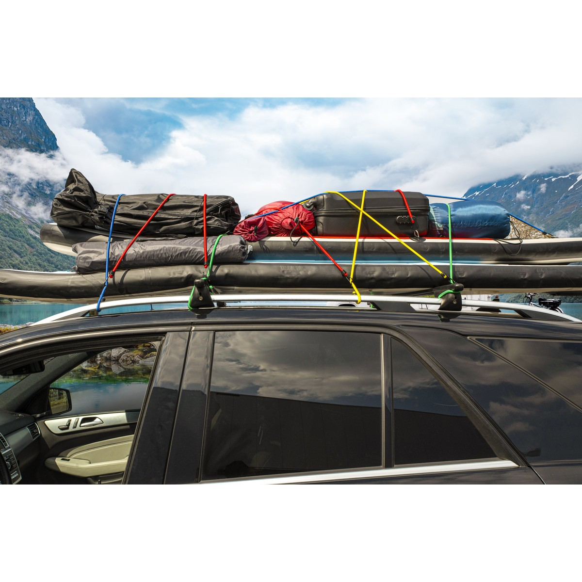 Zwarte auto met bagage op dakdrager, bergen en meer op achtergrond.