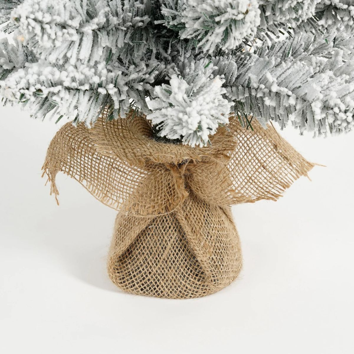 A small Christmas tree with snow covering, wrapped in burlap.