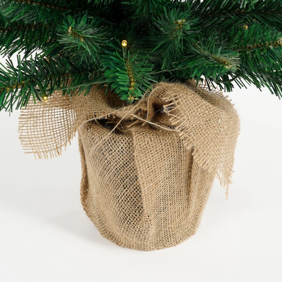 Close-up of a small green Christmas tree with burlap base and fairy lights.