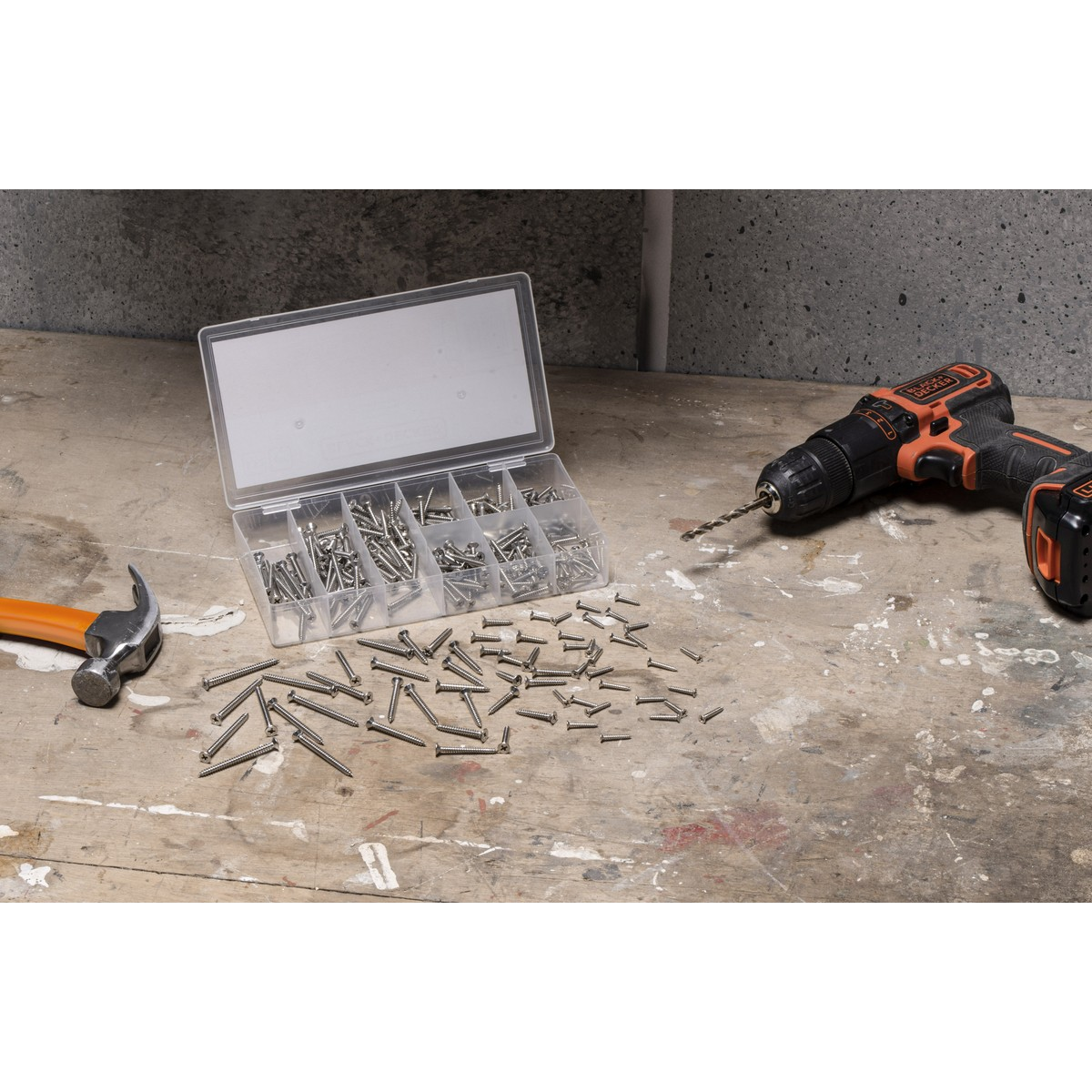 A hammer, a box of screws, and a cordless drill lie on a workbench.