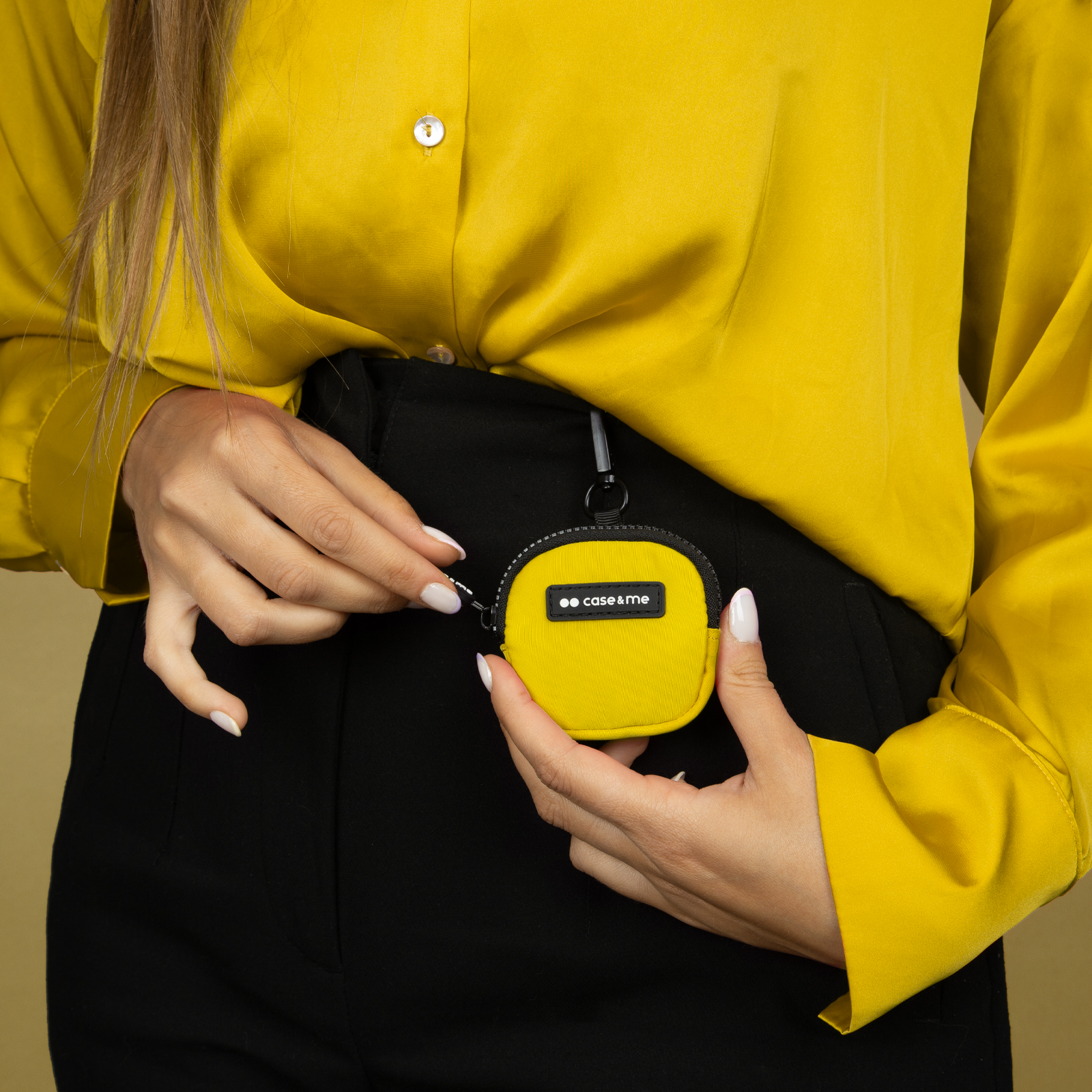 Una mujer con camisa amarilla y pantalones negros sostiene una pequeña bolsa amarilla.