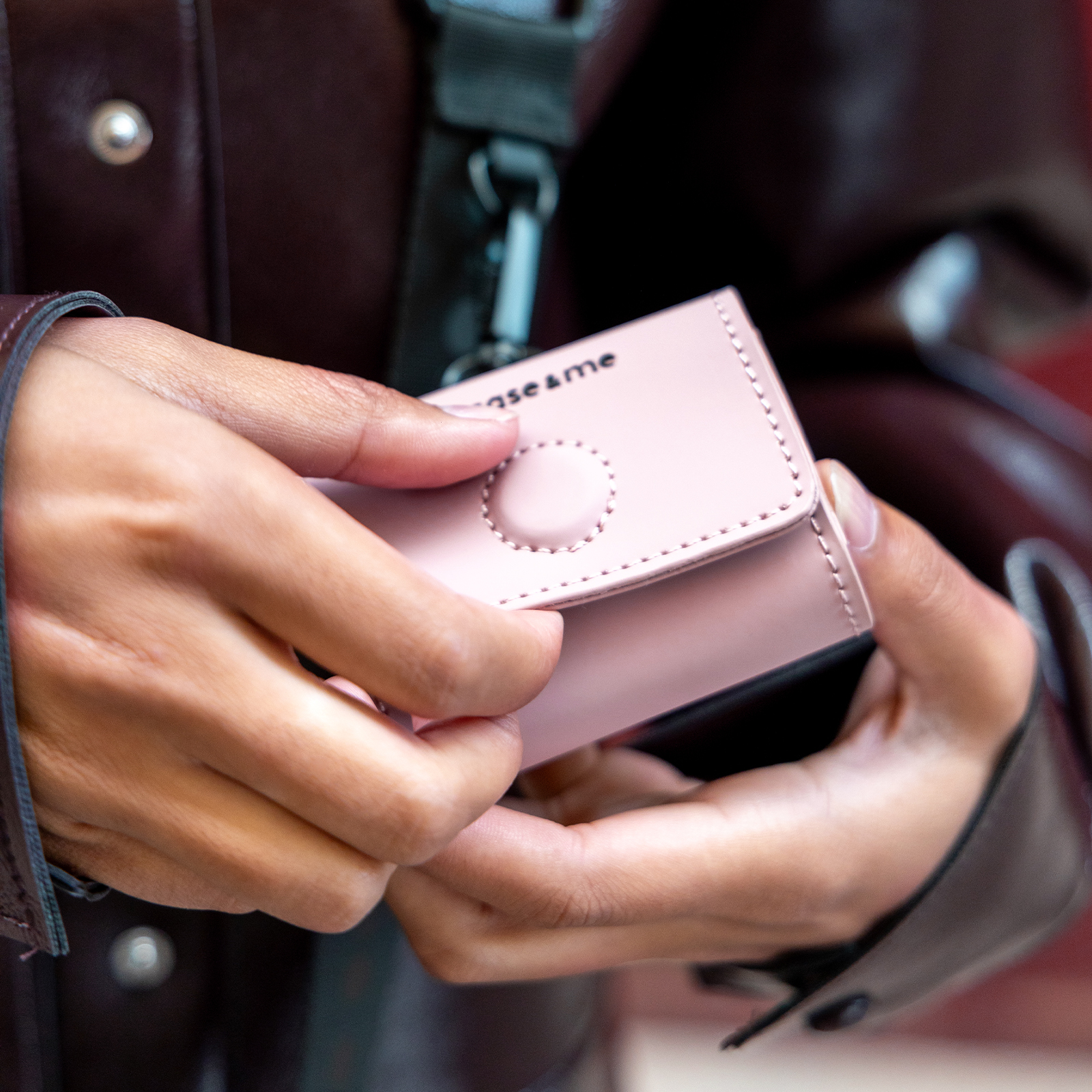 Manos sosteniendo una pequeña cartera rosa con costuras y un logo.