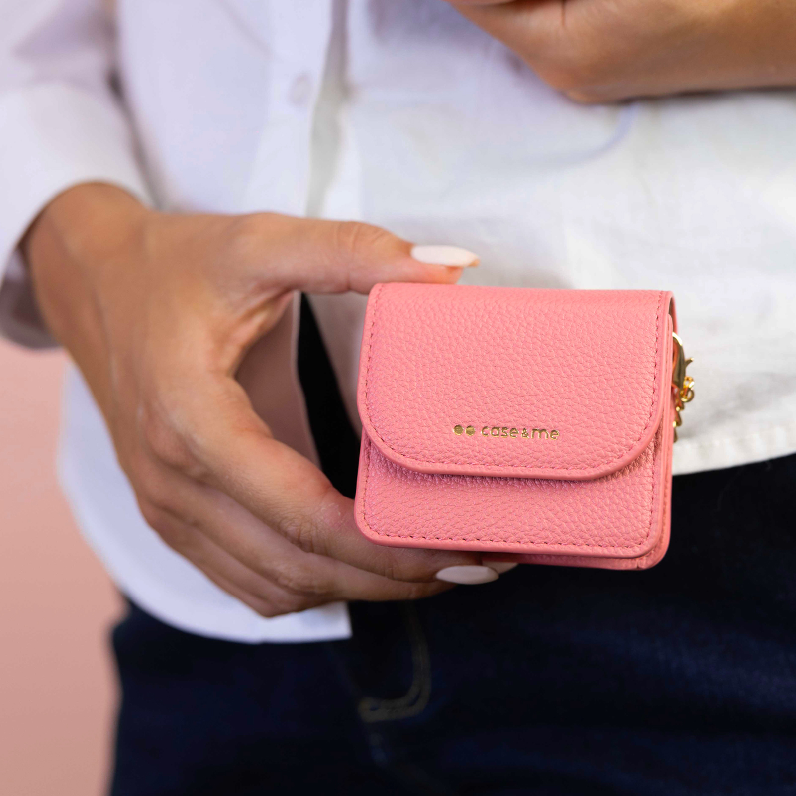 Una persona sostiene una cartera pequeña color coral con letras doradas y un dije.