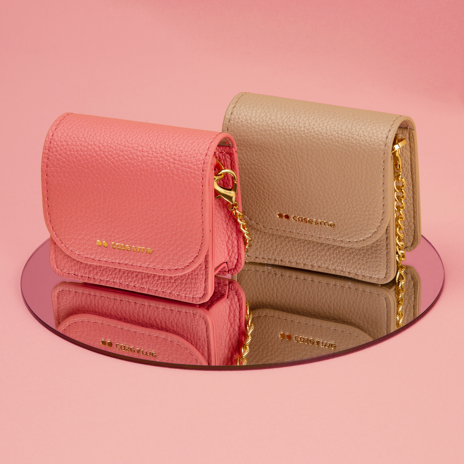 Dos pequeños bolsos de cuero texturizado, uno rosa coral, uno beige, con correas de cadena dorada sobre fondo rosa.