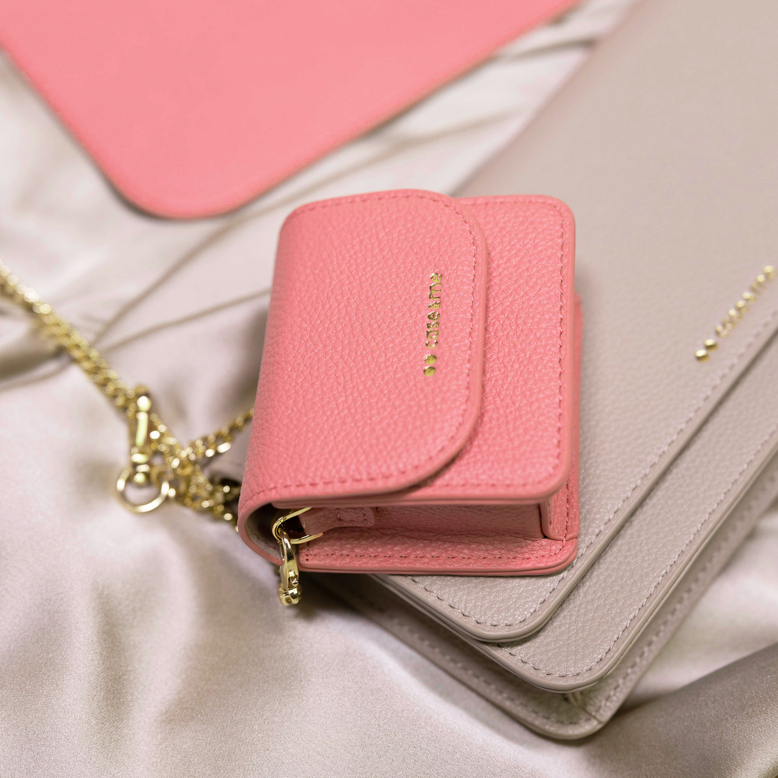 Un pequeño bolso rosa de cuero con detalles dorados descansa sobre un bolso gris más grande.