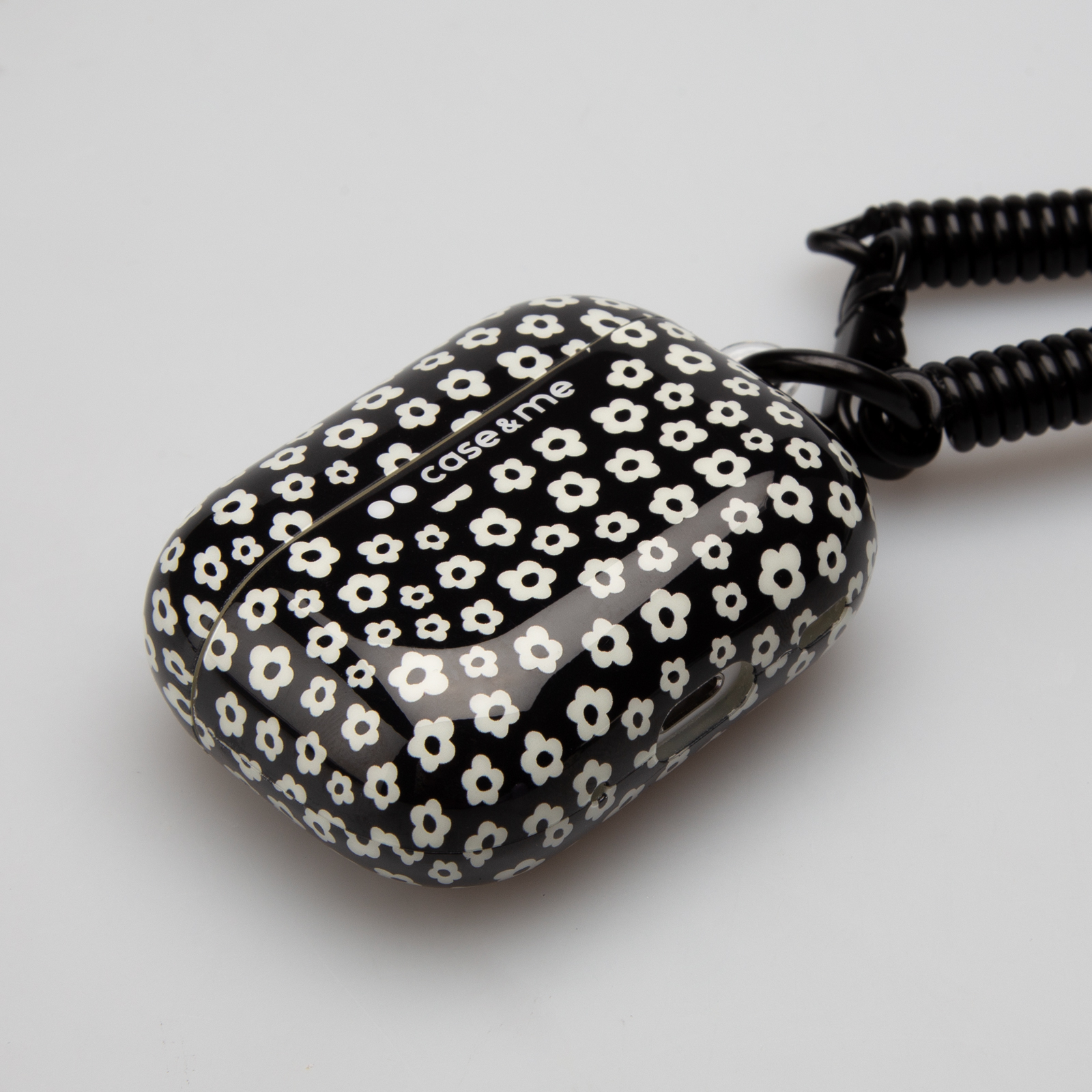 Funda negra para auriculares con estampado floral blanco, sujeta a un cordón en espiral.