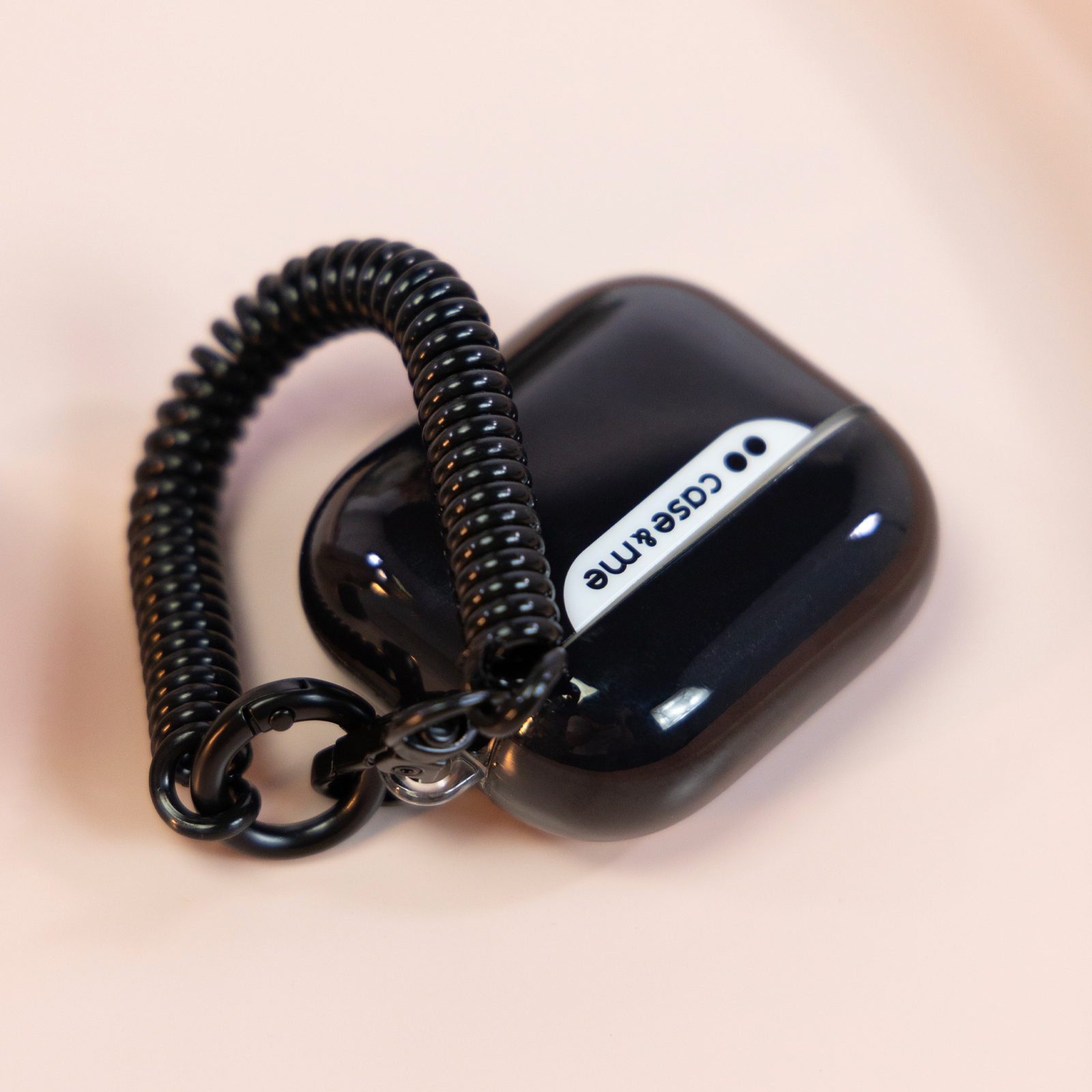 Funda negra con cable en espiral y mosquetón sobre fondo claro.