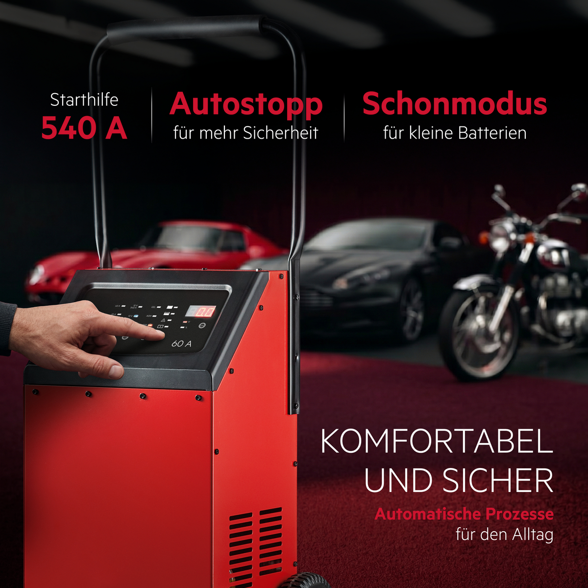 Rote Starthilfeeinheit mit Bedienerhand, Autos und Motorrad im Hintergrund.