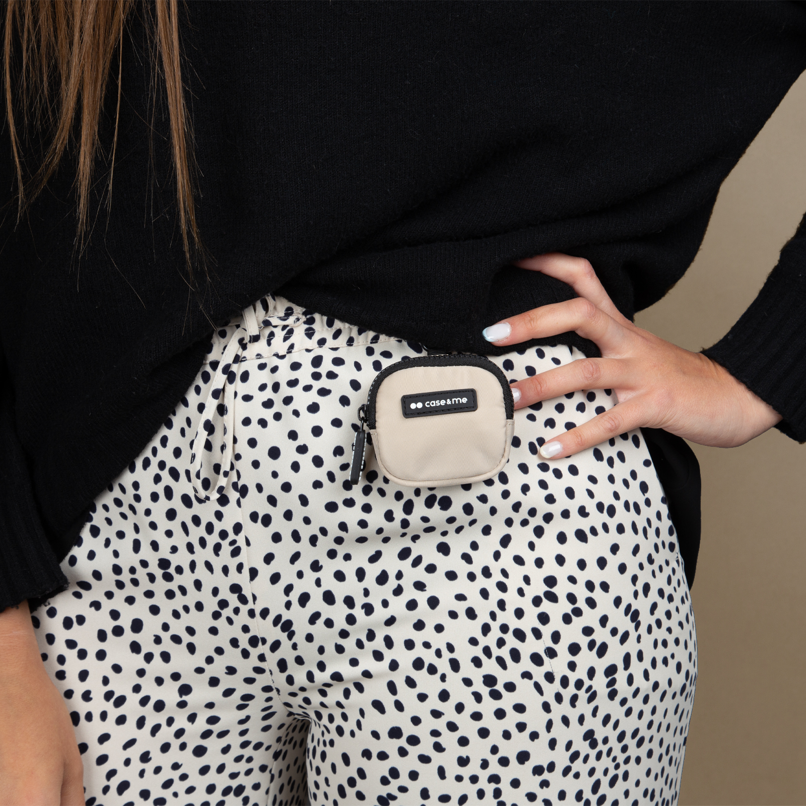 Una mujer viste un cárdigan negro y pantalones de lunares. Una pequeña bolsa beige está sujeta a sus pantalones.