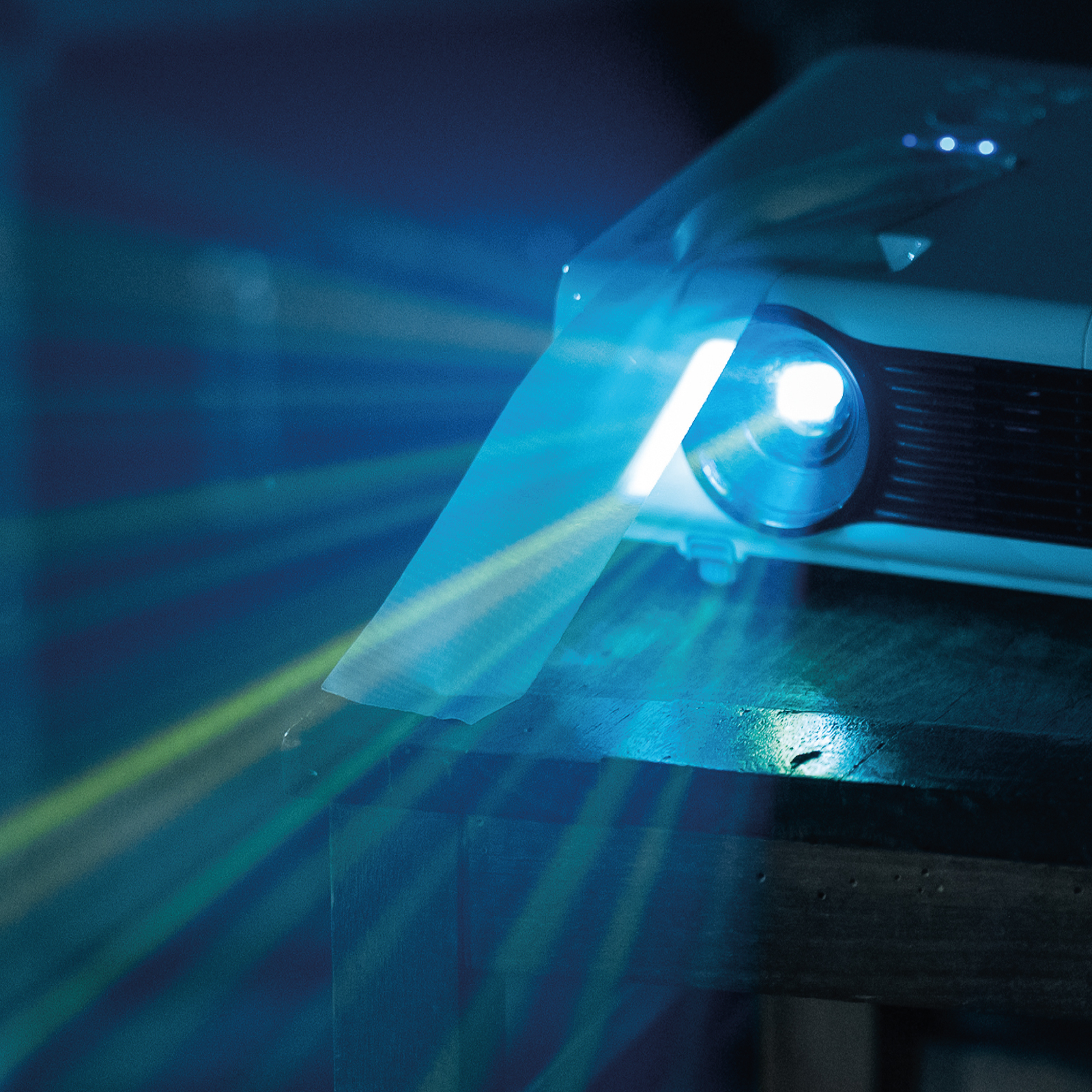 Un proyector proyecta rayos azul brillante y verde sobre una mesa de madera oscura.