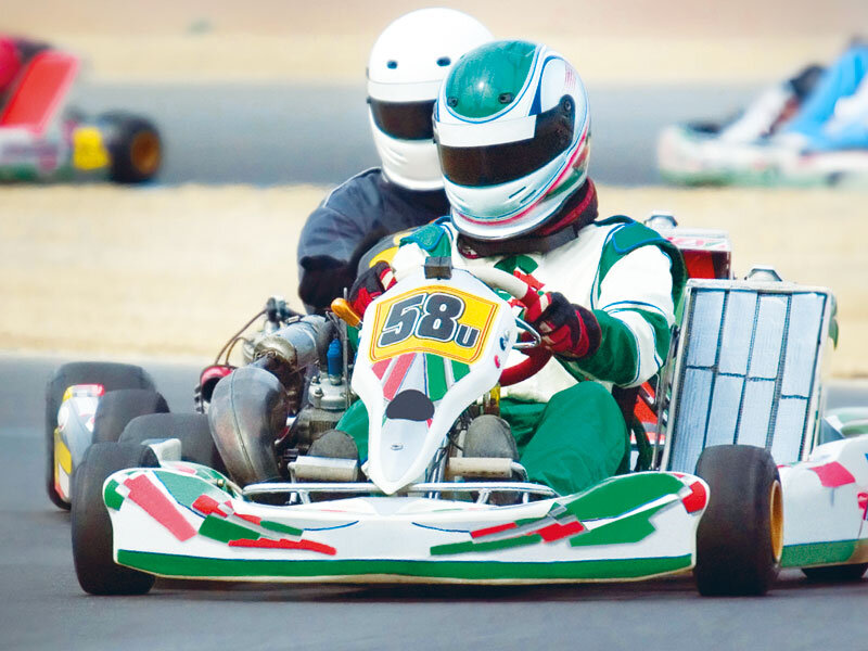 Dos karts compiten en una pista. El piloto delantero lleva casco verde.