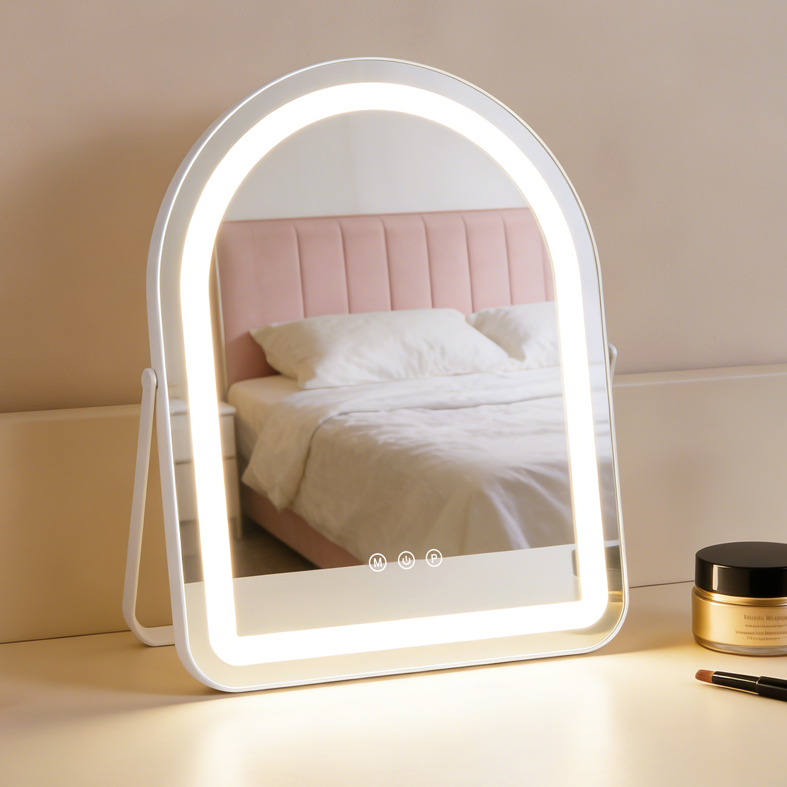 Un espejo de maquillaje iluminado sobre un tocador frente a una cabecera rosa y una cama.