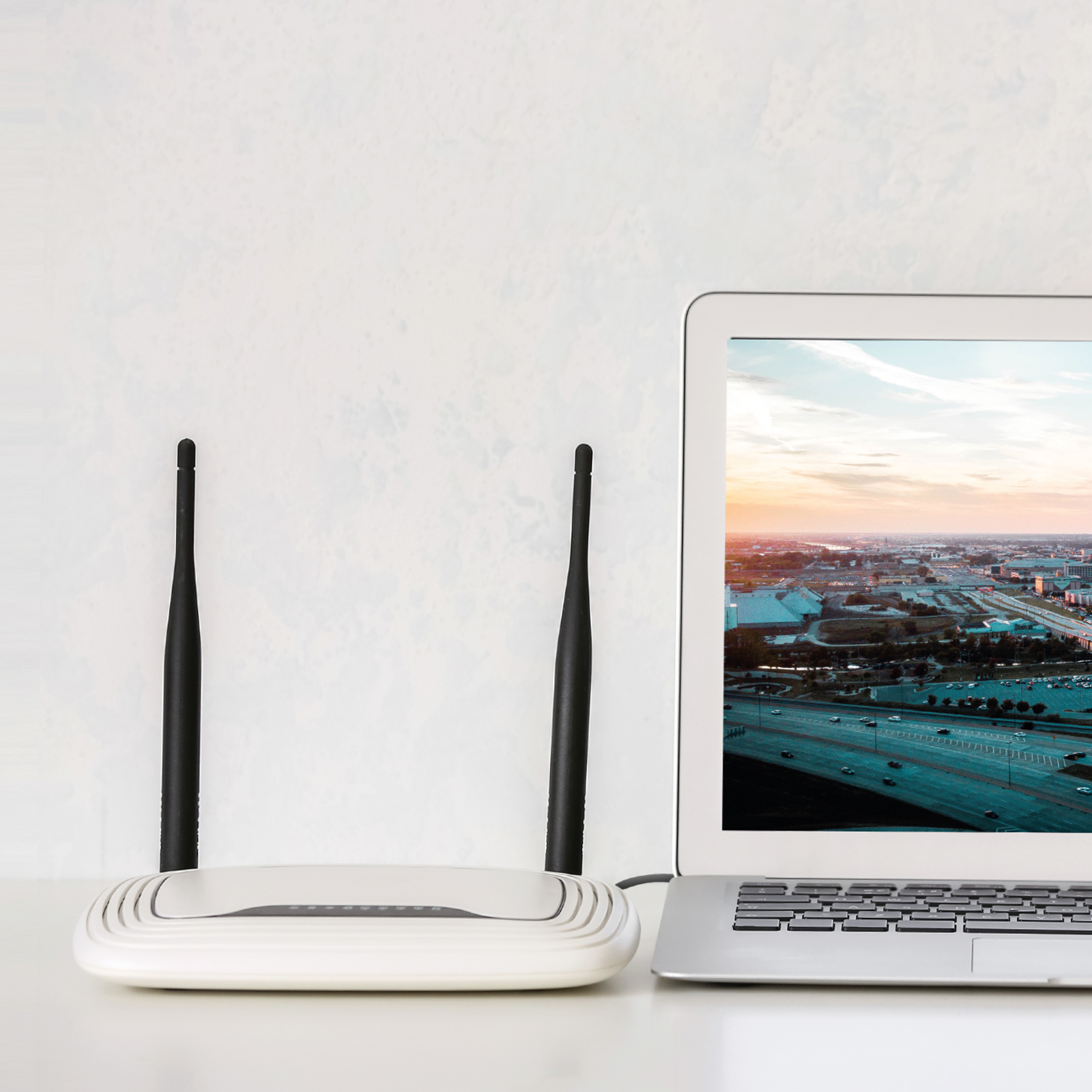 Un router blanco con dos antenas y un portátil mostrando una vista de ciudad en su pantalla.