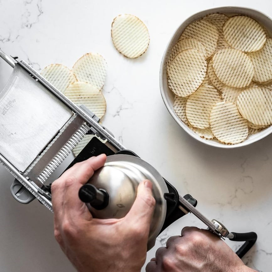 Eller, waffle kesim patates dilimlerini bir kaseye dilimlemek için mandolin dilimleyici kullanıyor.