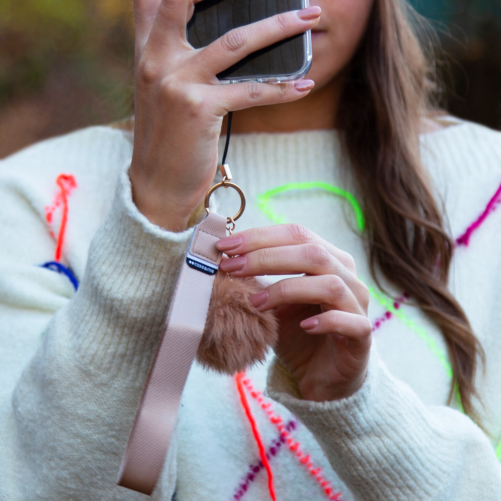 Una mujer sostiene un teléfono con un llavero de pompón marrón y una correa.
