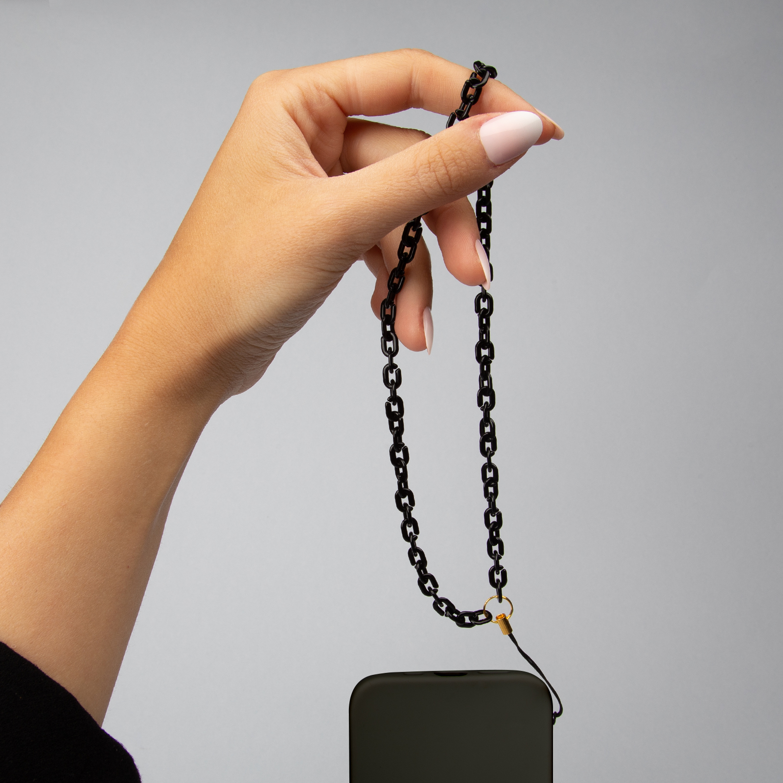 Una mano sostiene una cadena negra sobre un smartphone oscuro.