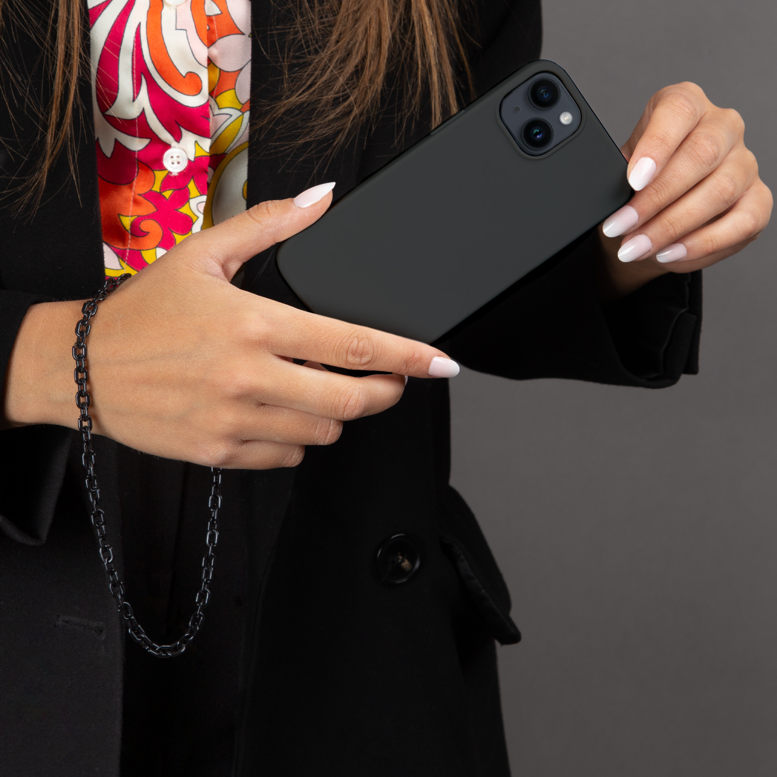 Una mujer de negro sostiene un smartphone negro. Lleva una blusa colorida.
